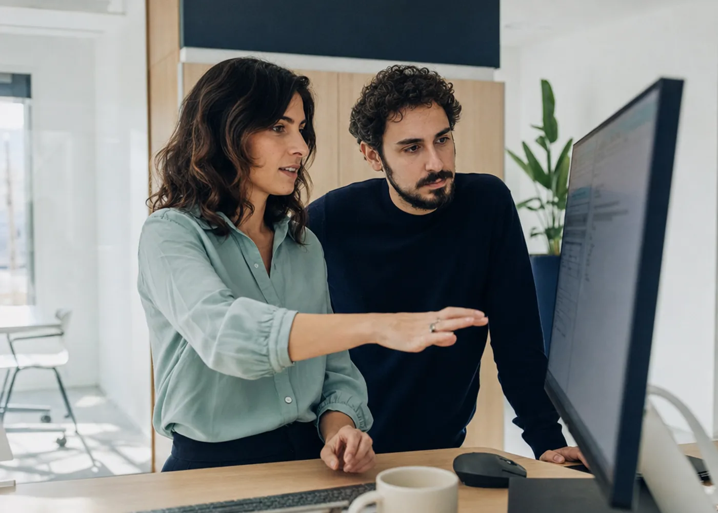 Dos compañeros revisan juntos un panel de datos en la pantalla de una oficina luminosa