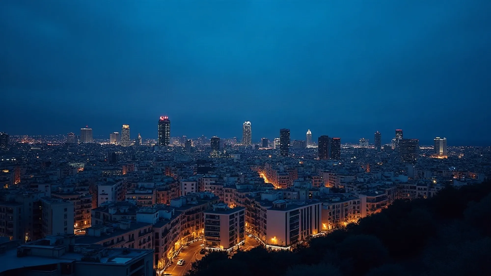Barcelona a hora azul vista desde una azotea, con cientos de ventanas encendidas sobre el cielo azul profundo.